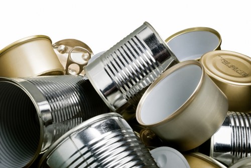 A collection of various metal cans, including silver, gold, and grey ones, some with opened or partially crushed lids, stacked closely together on a surface. The cans are primarily cylindrical with ribbed textures and smooth finishes, and they vary in size. The background is minimal, and the lighting highlights the metallic shine and reflective qualities of the containers. This image visually represents waste items suitable for rubbish removal services in Leytonstone, as provided by Garden Clearance Leytonstone, emphasizing the importance of proper disposal of metal packaging materials found in household or commercial rubbish collections.