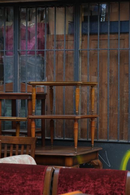 An orange upholstered armchair with a high, rounded backrest and wooden cabriole legs, positioned on a brick-paved sidewalk outdoors. The fabric has a subtle striped texture in shades of burnt orange 