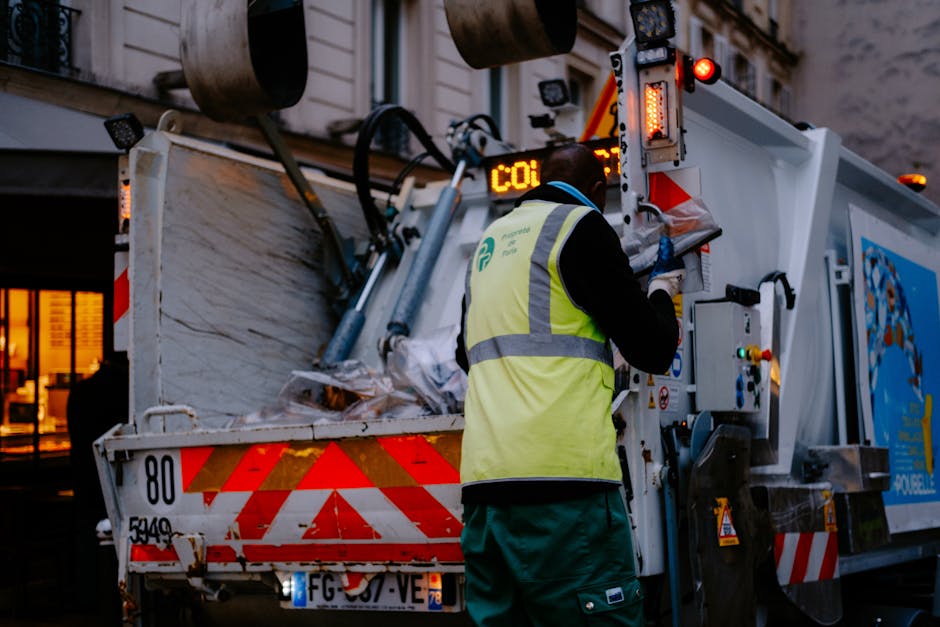 A large pile of discarded metal debris, including twisted and broken steel framework, crumpled sheets, and scattered fragments, is situated in front of a partially constructed or derelict building. Th
